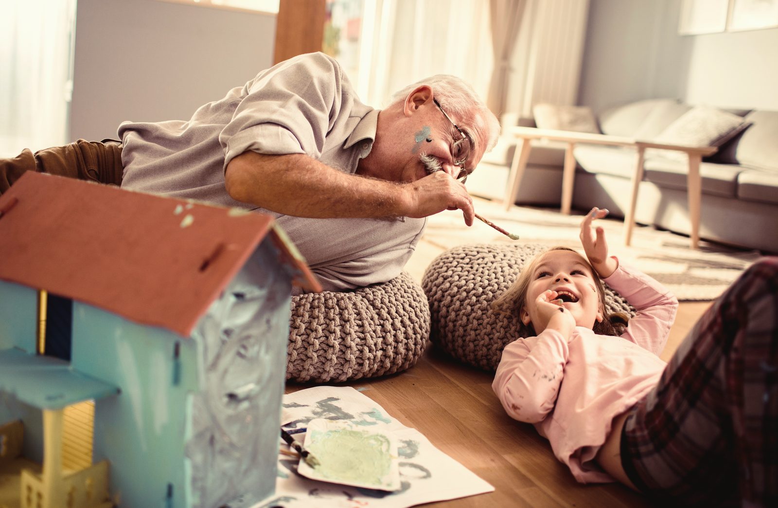 A grandfather painting a birdhouse with his laughing granddaughter